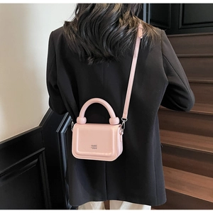 Détail du petit sac carré rose clair avec poignée arrondie et emblème du logo KISS SON