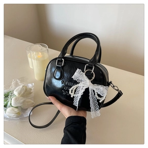 Détail du sac bowling noir brillant avec nœud en dentelle et breloque en perles