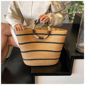 Detail of hand-woven straw tote with black stripes and circular handles for beach travel
