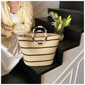 Straw beach bag with black stripes and woven handles in a summer vacation lifestyle setting