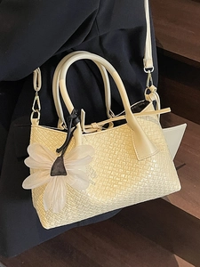 Elegant beige woven bucket bag featuring round handles and a delicate floral charm detail