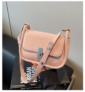 Close-up of pink matte leather crossbody bag with silver buckle held against a book