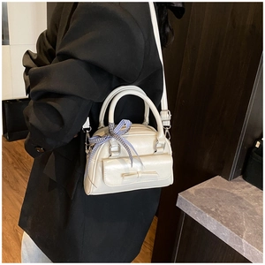 Détail du sac Boston crème avec nœud et ruban à carreaux porté par un mannequin