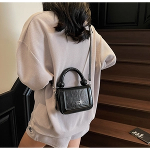 Détail du petit sac carré en cuir verni noir avec poignée à billes porté par le mannequin