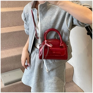 Détail du sac polochon en cuir verni rouge avec nœud et ruban à carreaux