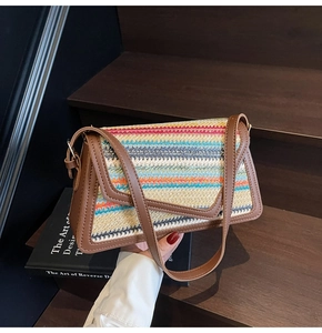 Detail of colorful rainbow straw woven crossbody bag with brown leather trim held by model