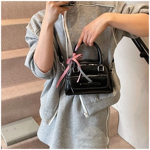 Détail d'un sac Boston noir brillant avec un nœud à carreaux rouges et des finitions argentées