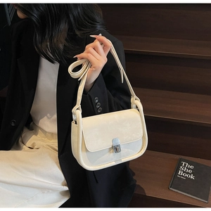 Detail of a creamy beige crossbody bag with silver rotating lock on a wooden staircase