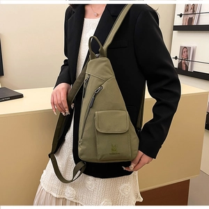 Detail of green canvas sling bag showing zipper closure and bunny print front pocket