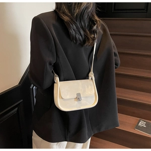 Detail view of cream square bag with silver clasp styled on black blazer outfit