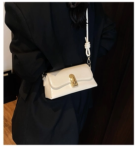 Detail of cream-colored crossbody bag with a gold metal clasp and knotted shoulder strap