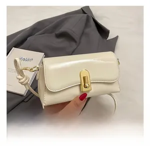 Close-up of cream rectangular shoulder bag with gold oval twist lock and knotted strap