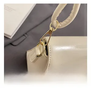 Close-up of golden metal hook on white patent leather baguette bag with stitching