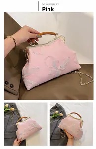 Detail of pink fabric handbag with floral embroidery, wooden handle, and gold chain strap