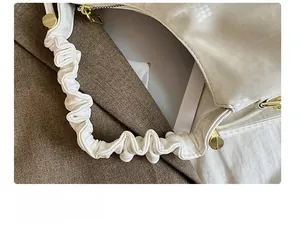 Detailed close-up of white embossed leather bag with pleated handle and golden hardware
