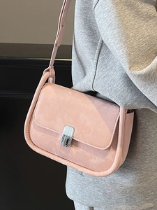 Pink suede crossbody bag with silver turn-lock clasp shown on shoulder of a model