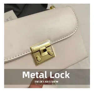 Close-up of golden wavy hardware lock on elegant beige leather crossbody bag details