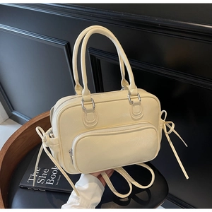Detail of cream leather handbag with front zip pocket and decorative side ribbon bows