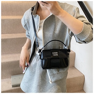 Detail of a black glossy woven crossbody bag shown on a model in a casual outfit