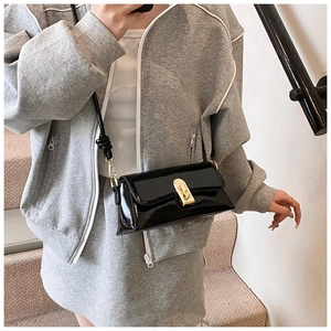 Detail of glossy black patent leather crossbody bag featuring a golden rectangular clasp