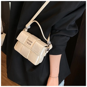 Detail of a beige woven square crossbody bag with metal logo and curved handle