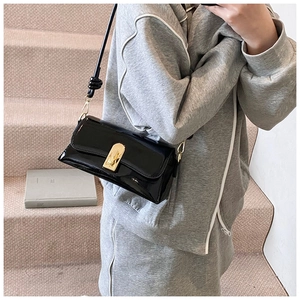 Detailed shot of black patent leather crossbody bag with elegant gold buckle and knot strap