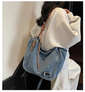 Blue denim tote bag with thick woven rope strap and silver hardware on a side model view