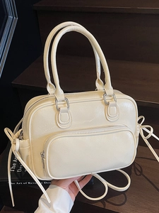 Minimalist cream patent leather Boston bag with bow details on dark brown stairs