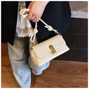 Detail of a creamy white glossy shoulder bag with a gold clasp and knotted strap design