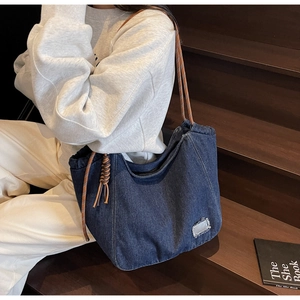 Detail of blue denim tote bag with brown braided rope straps on a lifestyle model