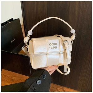Detail of cream woven handbag featuring beaded handle and metallic letter logo accent