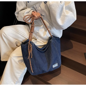 Detail of dark blue denim tote bag with brown woven rope shoulder strap and distressed patch