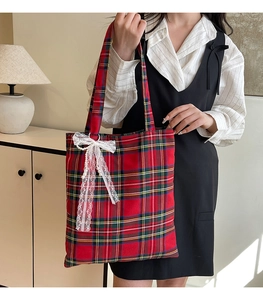 Close-up of red plaid tote bag featuring delicate white lace bow and pearl pendant detail