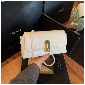 Detail view of cream patent leather bag with gold lock and thin shoulder strap