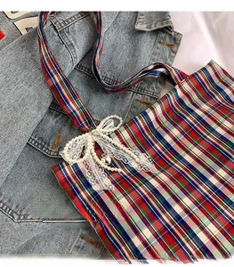 Detail of plaid tote bag featuring lace bow and pearl heart pendant on denim background