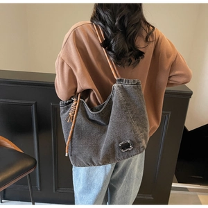 Rear view of model wearing a large grey washed denim tote bag with brown braided straps
