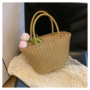 Dettaglio della borsa tote in paglia dorata con manici rotondi su sfondo pizzo