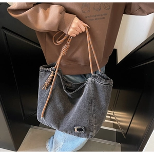 Detail of black denim tote bag with thick woven rope strap worn by a model in a stairwell