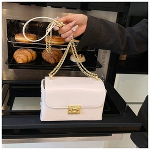 Detail of a creamy white leather shoulder bag with gold chain and metal lock closure