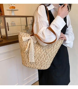 Detail showing woven straw texture and large white lace bow on chic shoulder tote bag