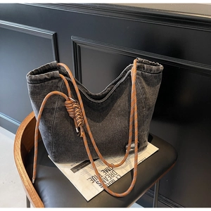 Detail of grey washed denim tote bag featuring orange braided rope straps and metal accents