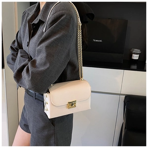 Chic cream crossbody bag with gold chain strap and rivet details shown on a model