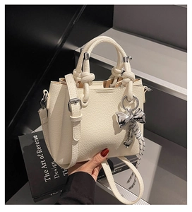 Detail view of white lychee pattern bucket bag with knot handles and silver bow charm