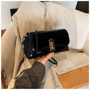 Detail of glossy black patent leather shoulder bag with elegant gold rectangular clasp