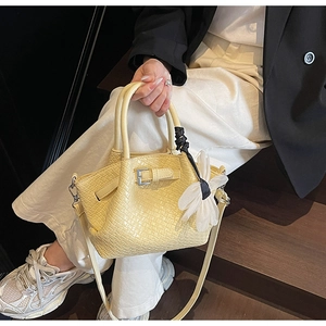 Détail d'un sac à main jaune tissé avec boucle et breloque fleurie translucide sur escalier