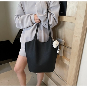 Close-up of black lychee grain tote bag with white cloud charm held by a model