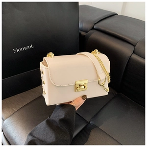Detail of a cream faux leather crossbody bag with a gold lock and chain strap