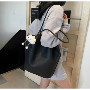 Detail view of black lychee grain tote bag with white fluffy cloud charm on shoulder