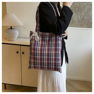 Detail view of plaid tote bag featuring lace bow and pearl charm against a cozy background