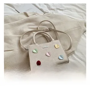 Détail du mini sac cabas en toile beige avec décor de cœurs colorés et logo en métal